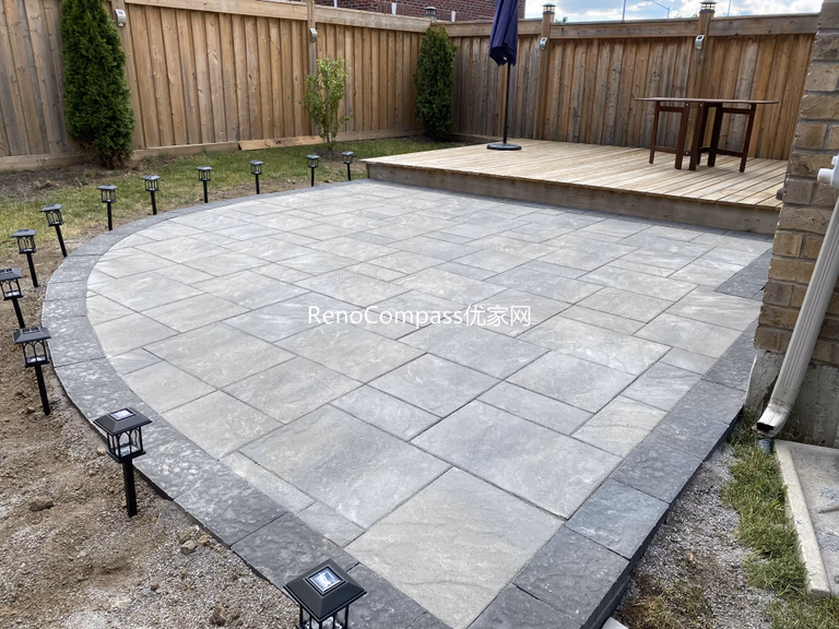 This Markham backyard renovation features a professionally installed interlocking stone patio with a smooth curved edge and contrasting stone border. Large-format gray pavers create a clean, modern surface that seamlessly connects to the raised wooden deck, enhancing both functionality and outdoor aesthetics. Designed for durability and low maintenance, this patio provides an elegant outdoor living space suitable for gatherings, relaxation, and everyday use.