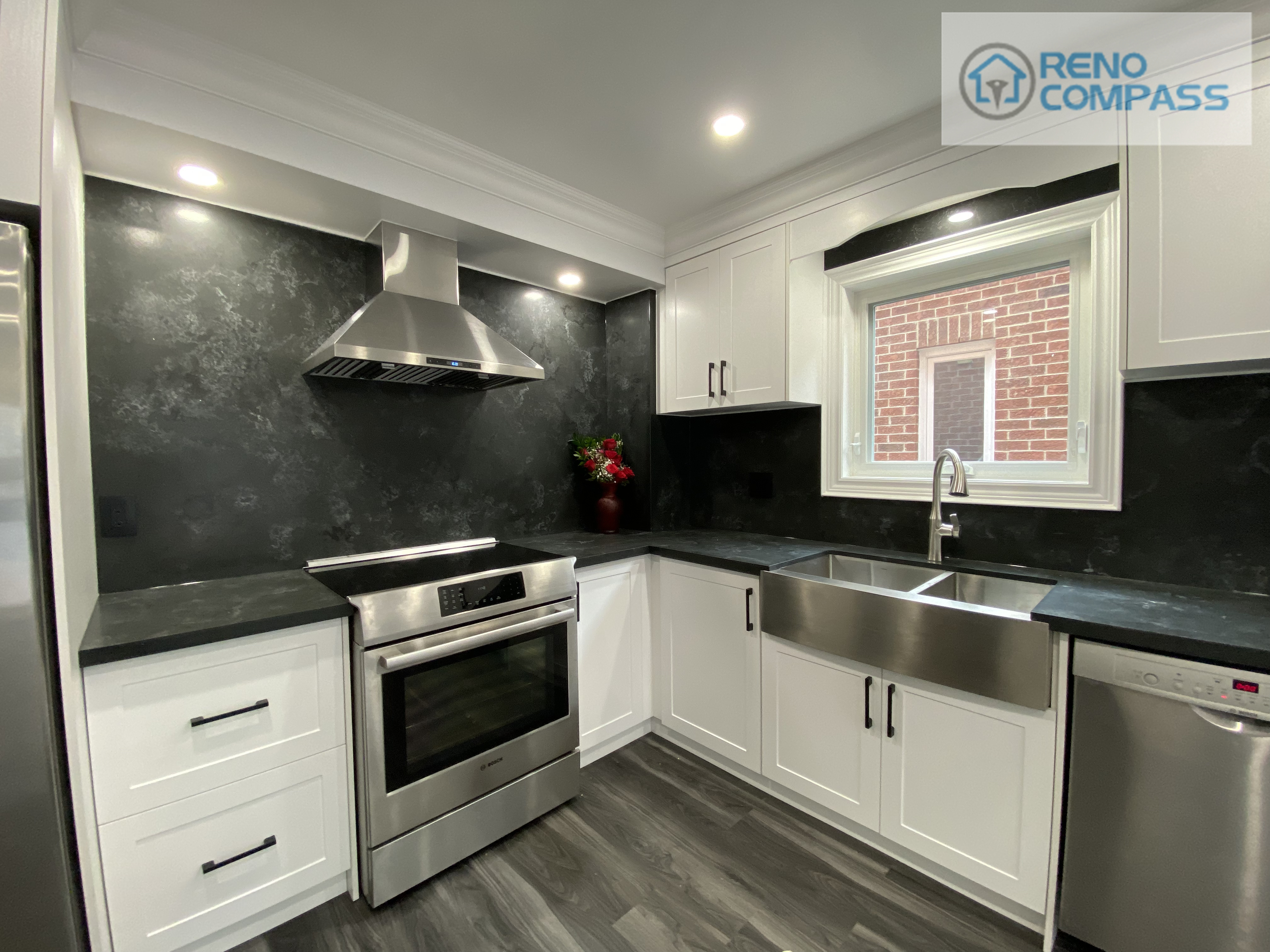 This modern kitchen interior renovation in Pickering features white shaker cabinets, black stone backsplash, quartz countertops, stainless steel appliances, and a farmhouse-style sink. Designed and built by Reno Compass Inc., this project showcases clean lines, efficient layout, and durable materials ideal for everyday family living.