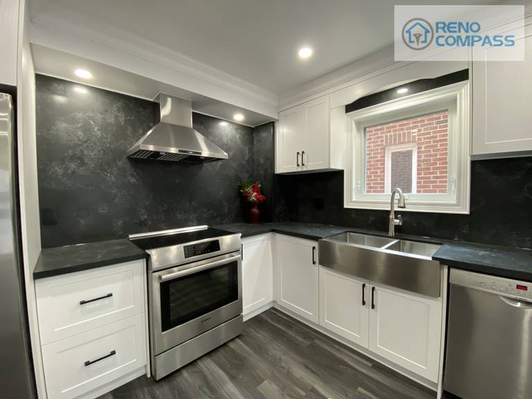 This modern kitchen interior renovation in Pickering features white shaker cabinets, black stone backsplash, quartz countertops, stainless steel appliances, and a farmhouse-style sink. Designed and built by Reno Compass Inc., this project showcases clean lines, efficient layout, and durable materials ideal for everyday family living.