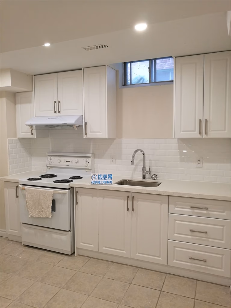 This image showcases a completed basement kitchen renovation in Markham, featuring clean white cabinetry, modern hardware, and a functional layout designed for basement living. The space includes a full set of upper and lower cabinets, durable countertops, and a practical cooking area with range hood and sink installation. Light subway-style backsplash tiles and neutral flooring create a bright and welcoming atmosphere, while the window above enhances ventilation and natural light. Completed by a professional Toronto Renovation Company, this basement kitchen upgrade focuses on efficient space planning, long-lasting materials, and modern finishes ideal for rental units, in-law suites, or extended family use.