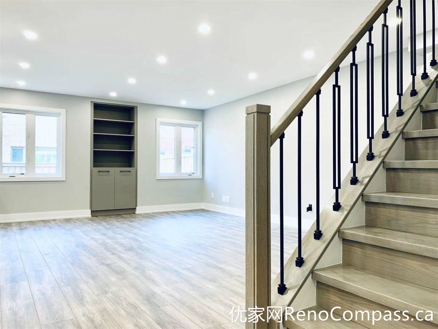 This Markham full home renovation features a bright open-concept basement with wood-look flooring, recessed pot lights, and a custom staircase with black metal railings. The clean layout and built-in shelving create a functional and inviting living area, ideal for family use or additional entertainment space.