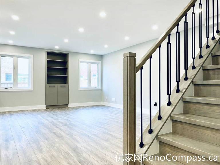 This Markham full home renovation features a bright open-concept basement with wood-look flooring, recessed pot lights, and a custom staircase with black metal railings. The clean layout and built-in shelving create a functional and inviting living area, ideal for family use or additional entertainment space.