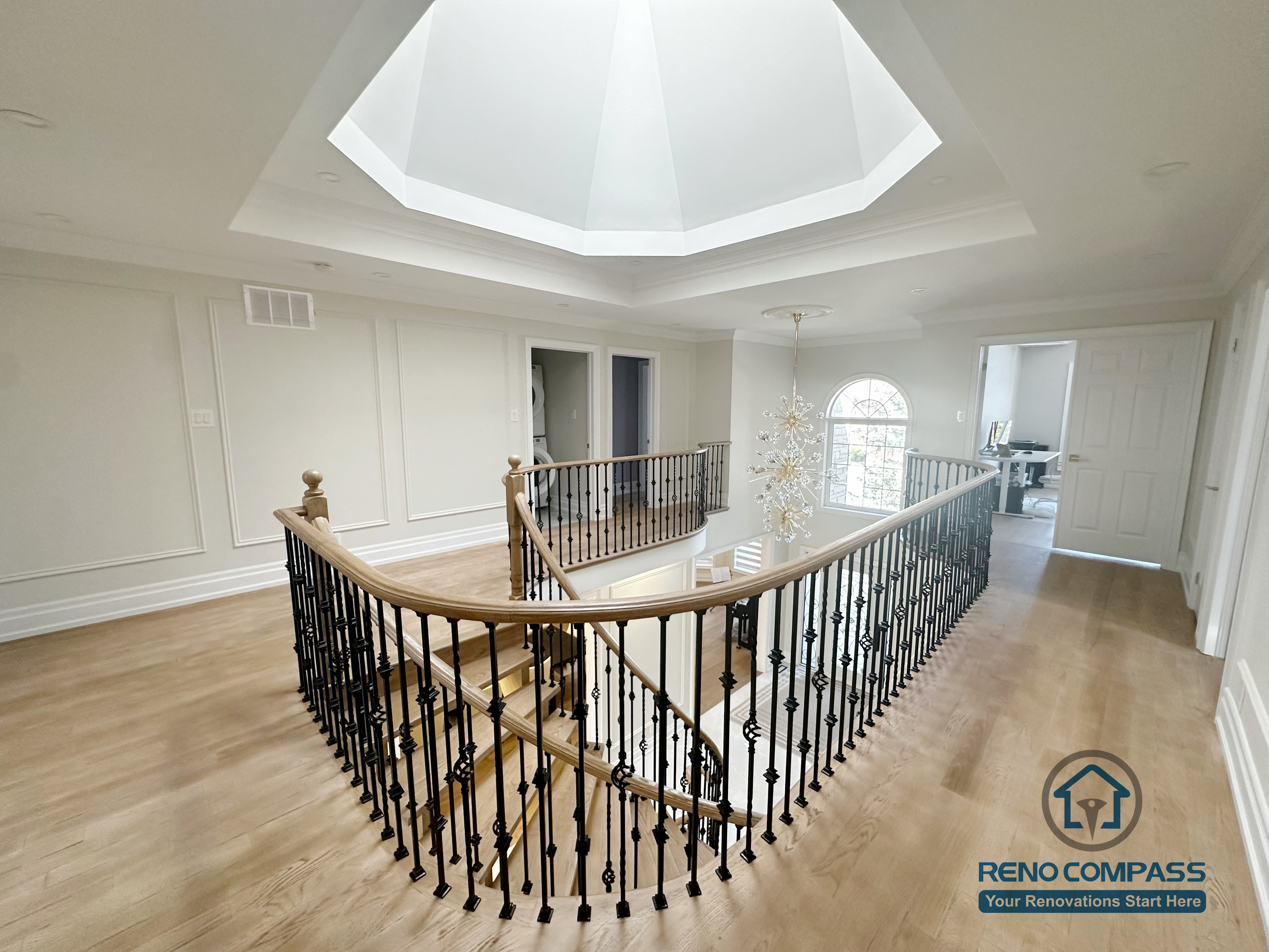 This image showcases a combined flooring and stair renovation completed in North York, featuring hardwood flooring on the upper level and a curved stair railing overlooking the main floor. The staircase is framed with decorative iron balusters and a smooth hardwood handrail, creating continuity between levels. Natural light from the overhead skylight enhances the warmth of the flooring and highlights the architectural detailing. This renovation demonstrates seamless coordination between flooring installation and stair design, improving both visual flow and spatial connection within the home.