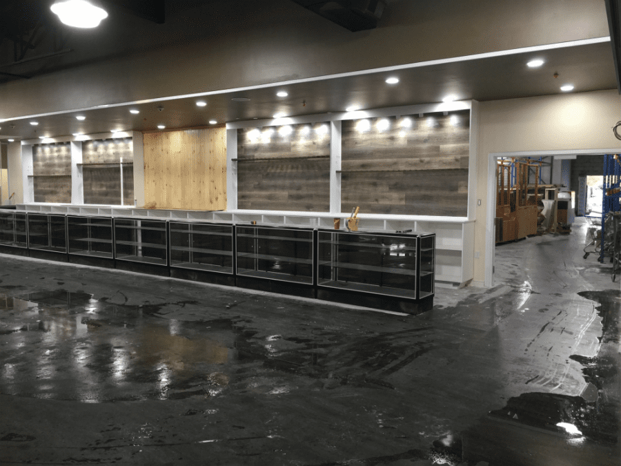 This image captures the construction phase of an outdoor retail store renovation, featuring structural ceiling framing, custom wood wall installation, and lighting preparation. The team is installing overhead framing and wood panel backdrops to support future retail displays and shelving systems. Reno Compass Inc. ensures precise craftsmanship and proper structural alignment during every stage of the commercial renovation process, building a durable and well-designed retail environment from the ground up.
