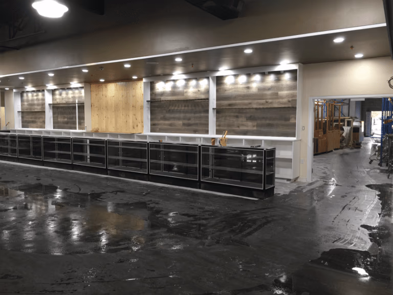 This image captures the construction phase of an outdoor retail store renovation, featuring structural ceiling framing, custom wood wall installation, and lighting preparation. The team is installing overhead framing and wood panel backdrops to support future retail displays and shelving systems. Reno Compass Inc. ensures precise craftsmanship and proper structural alignment during every stage of the commercial renovation process, building a durable and well-designed retail environment from the ground up.