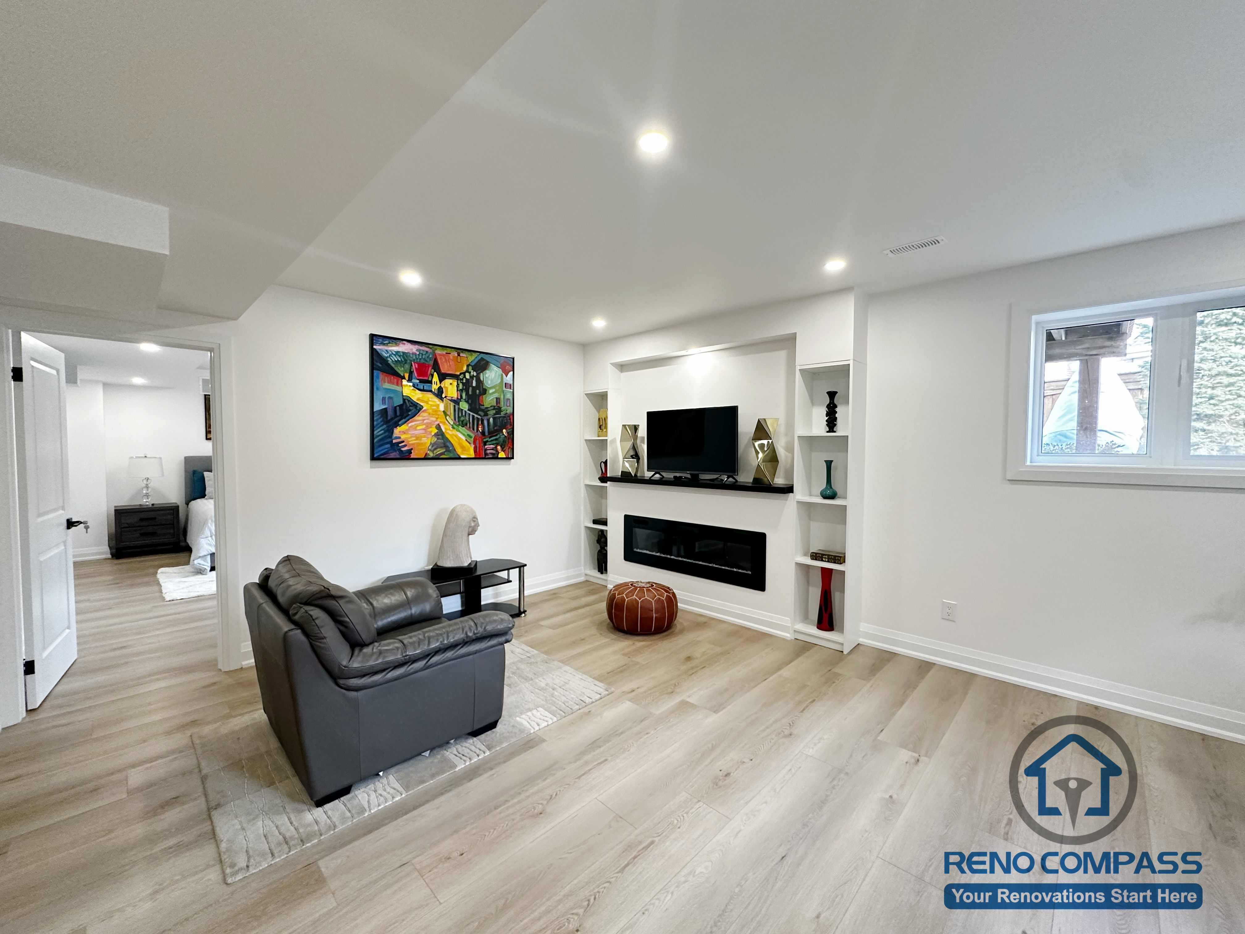 This Richmond Hill basement renovation features a finished living room designed as a flexible family gathering space. The layout includes a custom built-in media wall with integrated shelving and a linear fireplace, paired with recessed ceiling lighting for even illumination. Wide-plank flooring suitable for basement conditions enhances durability while maintaining a clean, cohesive appearance. The open layout allows for multiple furniture arrangements and supports everyday living, entertainment, or guest use within the basement level.