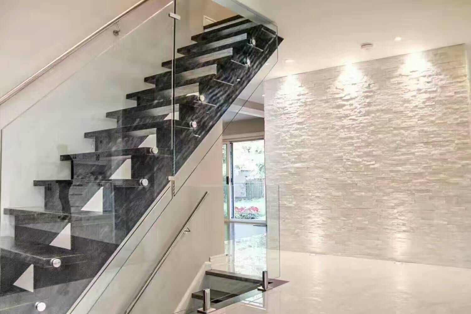 This Markham interior renovation highlights a modern staircase design with dark stone treads, frameless glass railing, and stainless steel hardware. The staircase is paired with a textured stone feature wall and integrated recessed lighting, creating a bright and open atmosphere. Light marble-look flooring enhances reflection and visual continuity throughout the space. Designed to improve both safety and aesthetics, this staircase renovation adds architectural impact and long-term value to the home. Completed by a professional Toronto renovation contractor.