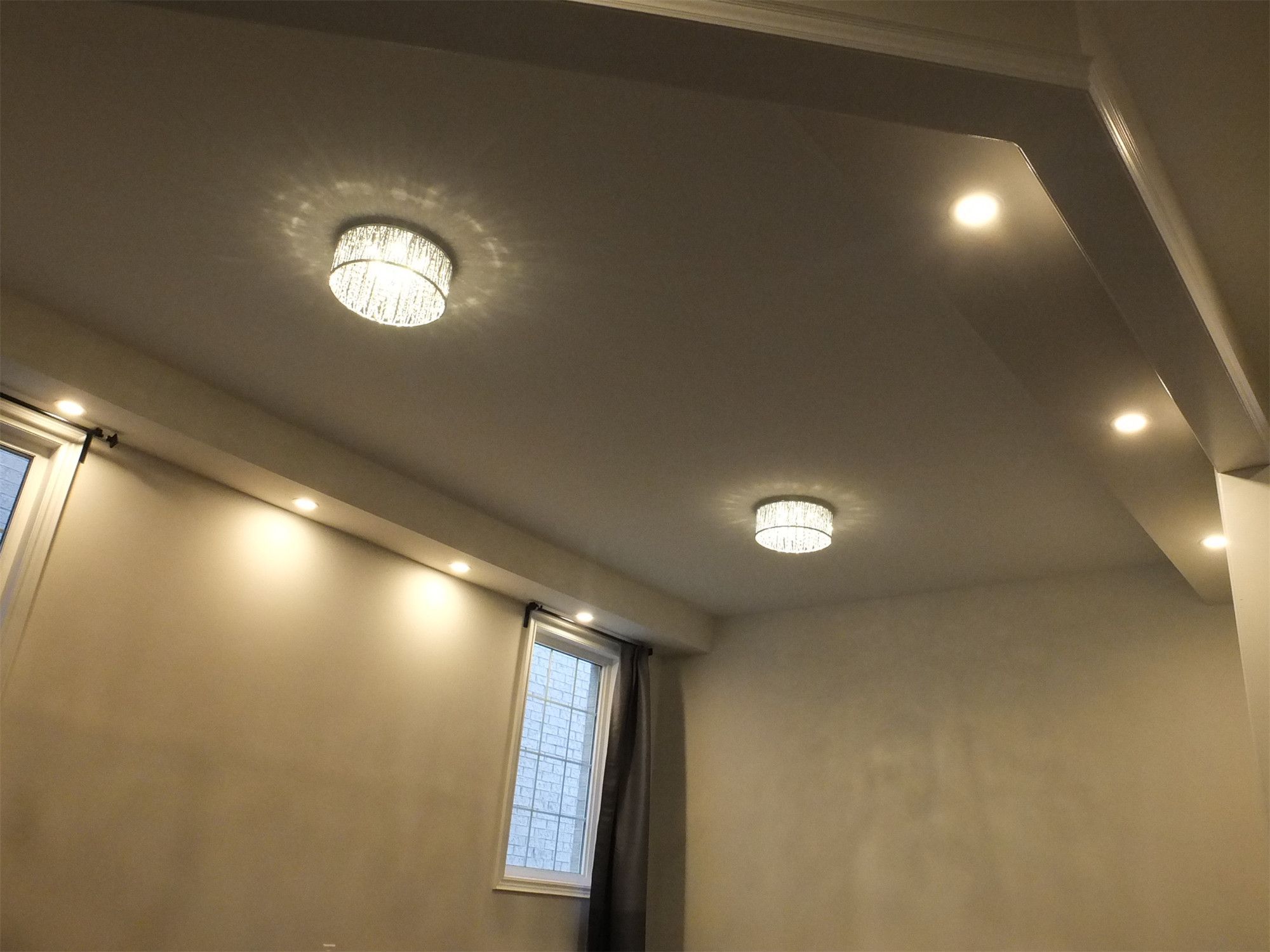 This Kleinburg interior renovation showcases a clean and modern ceiling design featuring recessed pot lights and elegant ceiling fixtures. The layered lighting layout enhances brightness and creates a warm, inviting atmosphere throughout the living space. Combined with smooth ceiling finishes and natural light from nearby windows, the lighting design adds both functionality and contemporary style to the renovated interior.