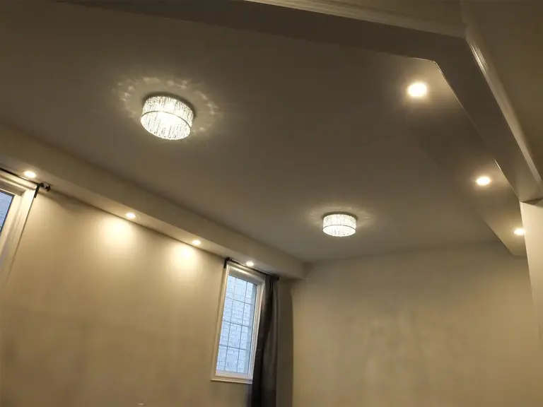 This Kleinburg interior renovation showcases a clean and modern ceiling design featuring recessed pot lights and elegant ceiling fixtures. The layered lighting layout enhances brightness and creates a warm, inviting atmosphere throughout the living space. Combined with smooth ceiling finishes and natural light from nearby windows, the lighting design adds both functionality and contemporary style to the renovated interior.