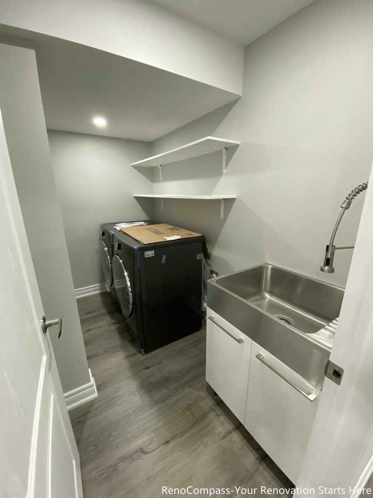 This Oakville basement renovation features a modern laundry room with upgraded flooring, a stainless steel utility sink, and custom wall shelving for efficient storage. The clean layout maximizes functionality while maintaining a bright and organized workspace for daily use. Designed and completed by a trusted Toronto renovation company, this basement laundry upgrade improves convenience, durability, and overall home value while creating a practical and well-designed utility space.
