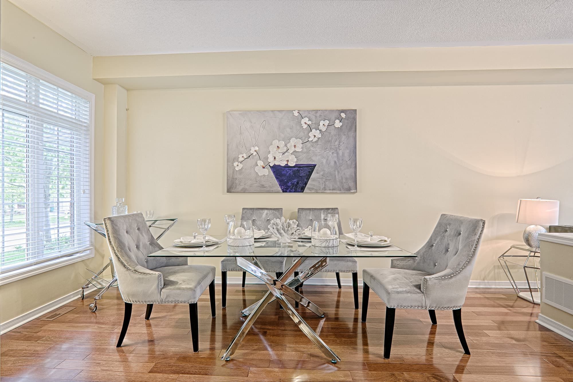 This elegant dining table setting highlights a simple and lovely interior design with a clean open layout and refined staging details. The glass tabletop, upholstered dining chairs, and neutral color palette create a light and sophisticated atmosphere. The long visual axis enhances depth and openness, making the space feel bright, balanced, and suitable for everyday dining and entertaining in modern family homes.