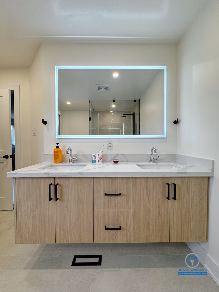 This Richmond Hill bathroom renovation features a modern double vanity with a floating wood cabinet, integrated storage, and a backlit mirror that enhances both functionality and visual balance. Clean lines, neutral finishes, and thoughtful lighting design create a bright, refined space suitable for daily family use. Completed as part of a Toronto renovation project focused on durability, comfort, and timeless interior design.