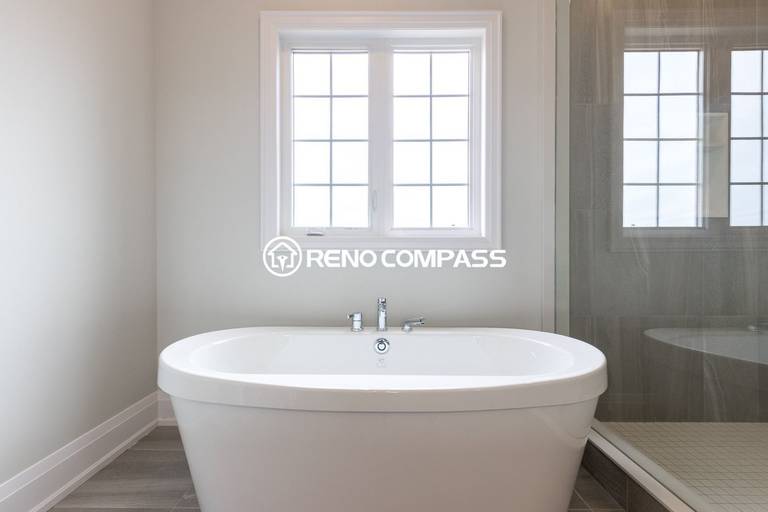 Elegant bathroom renovation in Newmarket featuring a modern freestanding bathtub, large window for natural light and a glass shower enclosure. Completed by a professional Toronto renovation company, this bathroom design creates a relaxing and luxurious spa-like atmosphere for the homeowner.