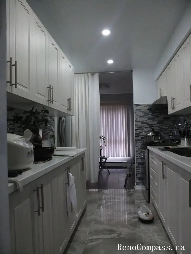This North York interior renovation features a clean and functional galley-style kitchen with custom full-height cabinetry, modern hardware, and a sleek stone-look floor. The narrow layout is carefully optimized to improve workflow, storage efficiency, and lighting, creating a bright and practical kitchen space suitable for daily use in Toronto homes.