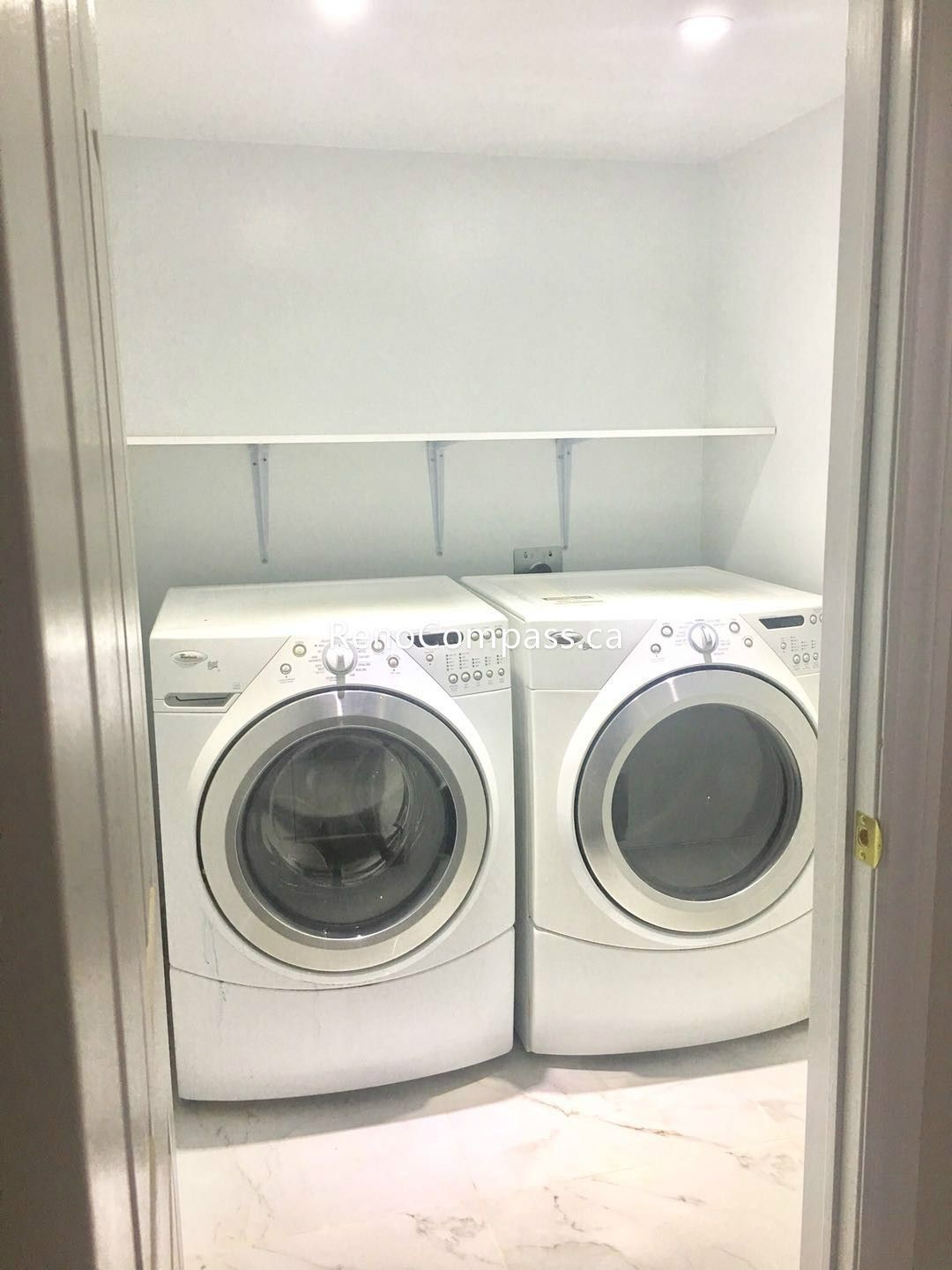 This Toronto basement renovation includes a newly finished laundry room with modern front-load washer and dryer units, durable tile flooring, and clean built-in shelving for storage. The bright lighting and organized layout create a practical and efficient laundry space. Completed by Reno Compass Inc., this basement upgrade enhances convenience, functionality, and overall home value for Toronto homeowners.