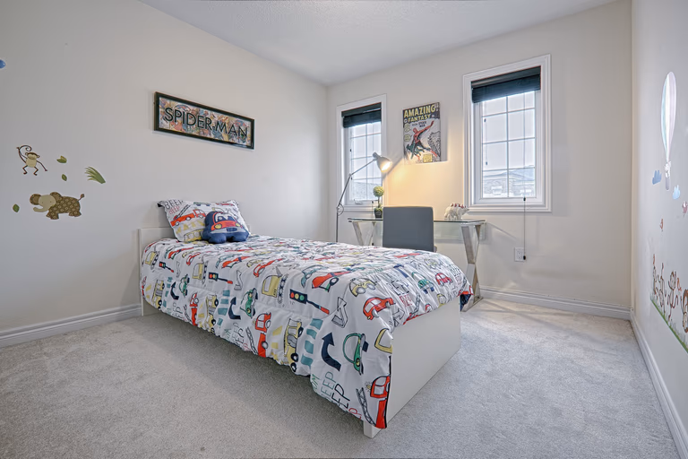 This bright and functional kids’ bedroom renovation features soft neutral walls, plush carpeting, and large windows that allow natural light to enhance the space. The layout includes a cozy bed setup with playful décor and a compact study desk positioned by the window to maximize productivity and comfort. Designed to balance practicality and style, this bedroom upgrade reflects the quality craftsmanship of a professional Toronto renovation company specializing in modern residential interior transformations.