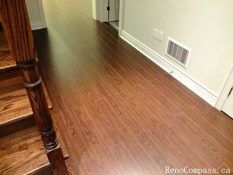 Newly installed dark walnut laminate flooring completed during an interior renovation project in Richmond Hill. The renovation features clean white baseboards, smooth wall finishes, and seamless flooring transitions beside the staircase, creating a warm and elegant hallway space. Completed by Reno Compass Inc., a trusted Toronto renovation company specializing in flooring upgrades and interior home renovations.