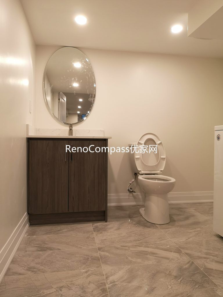Newly renovated Richmond Hill basement bathroom featuring modern tile flooring, custom vanity cabinet, round mirror, and upgraded lighting. This basement renovation by Reno Compass Inc. enhances functionality, brightness, and modern comfort for everyday use.