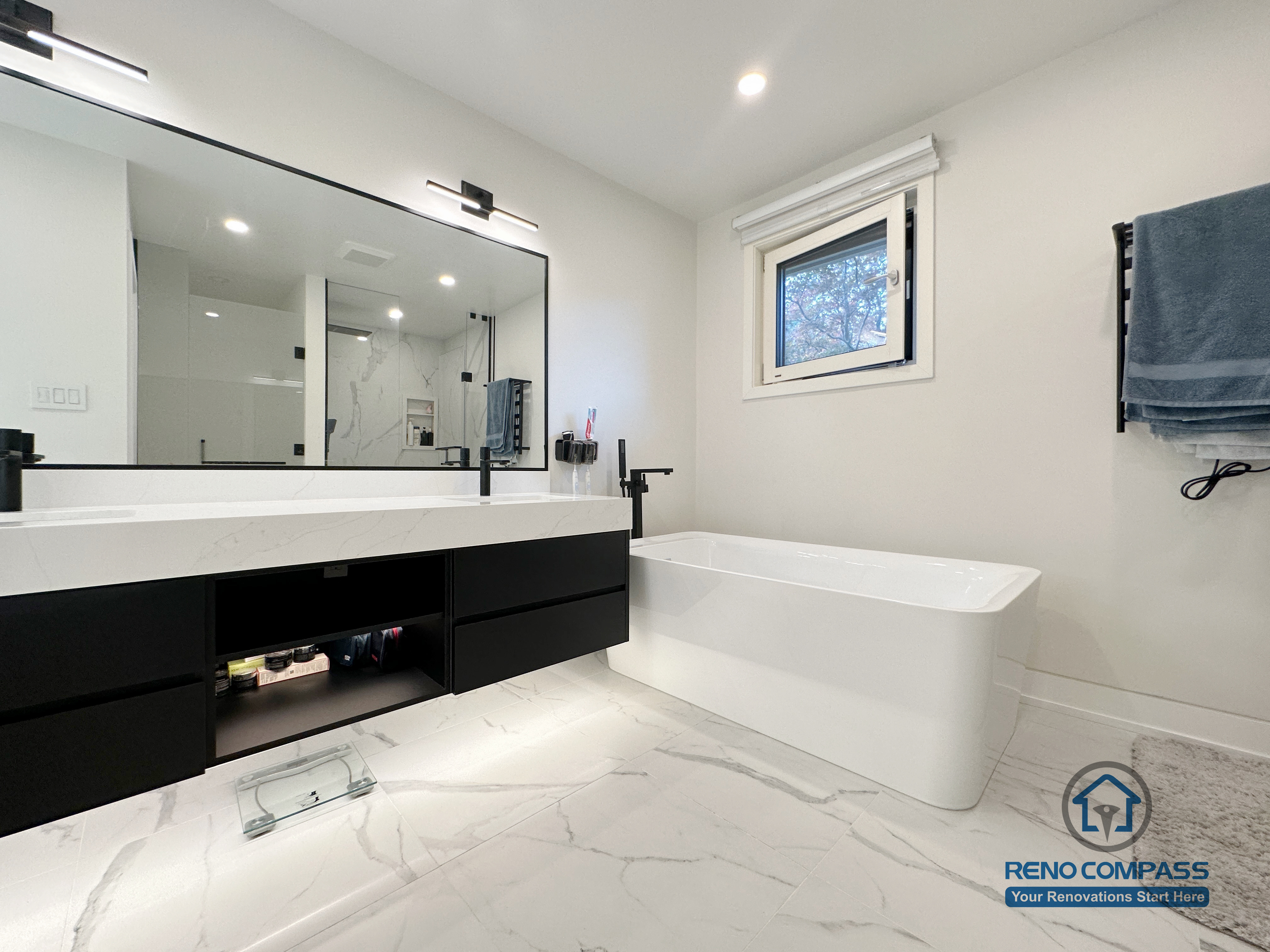 Modern bathroom renovation in Toronto featuring a sleek freestanding bathtub, floating custom vanity with integrated storage, oversized mirror, matte black fixtures, and marble-look porcelain flooring. Completed by an experienced Toronto renovation company with attention to comfort, layout, and clean modern aesthetics.