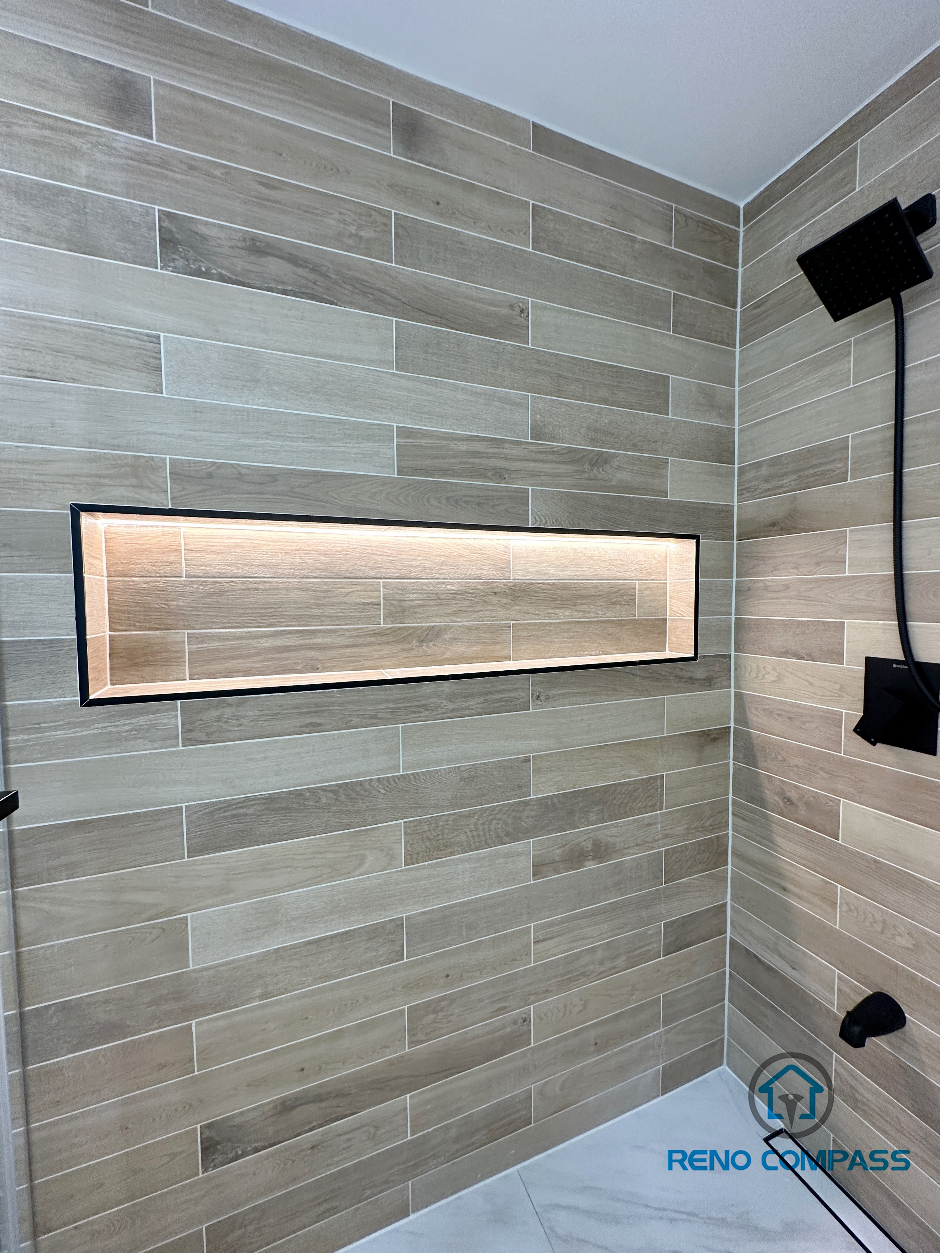 Modern bathroom renovation in Vaughan featuring a custom-built horizontal shower niche with integrated LED lighting. The shower wall is finished with wood-look porcelain tiles laid in a clean horizontal pattern, paired with matte black shower fixtures for a contemporary spa-style design. This project showcases detailed craftsmanship by a professional Toronto renovation company, combining functional storage with elegant lighting and premium tile installation.