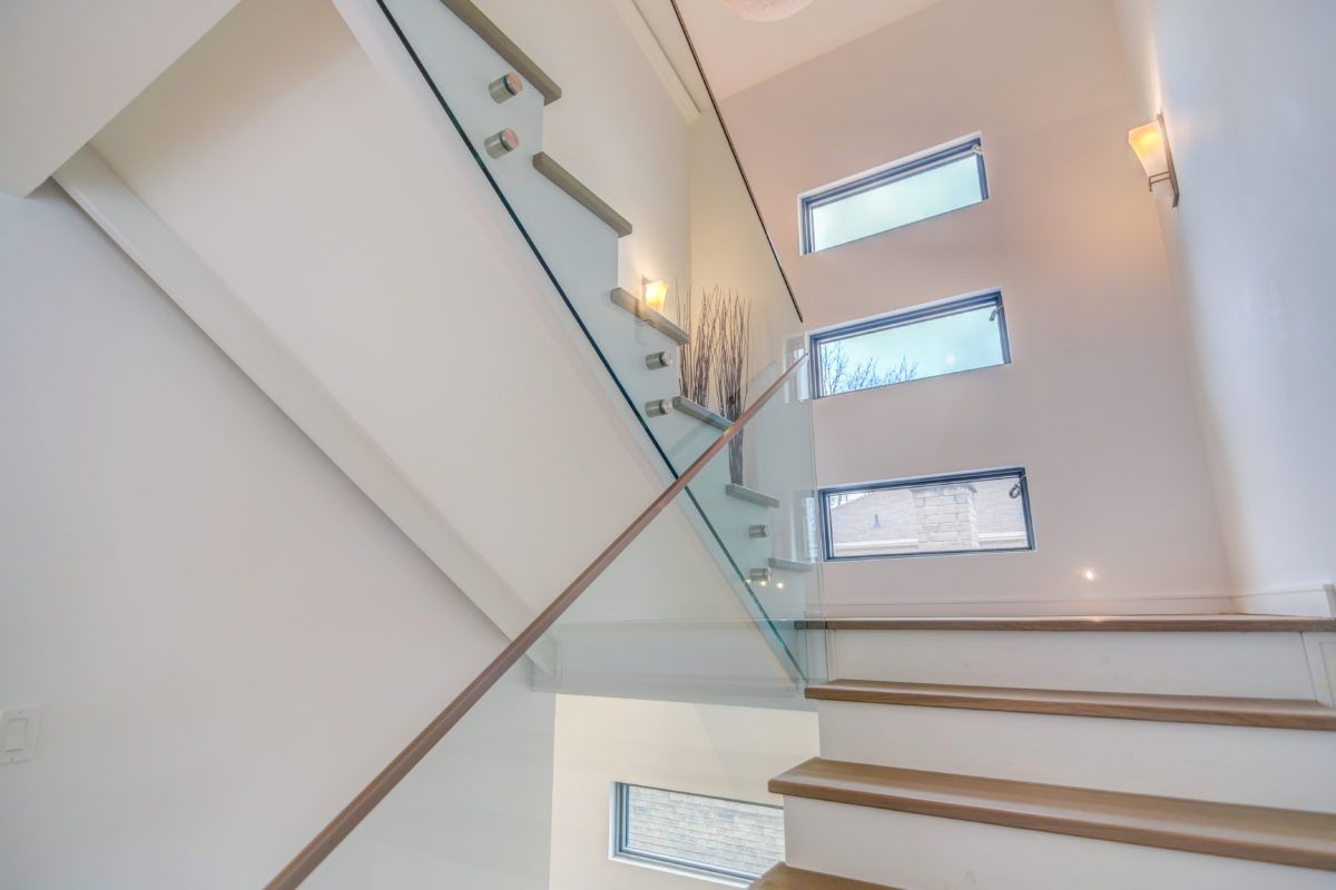Modern staircase renovation in a Toronto luxury home featuring solid wood steps, frameless glass railing, and tall vertical windows that bring in abundant natural light. The clean white walls, minimalist design, and contemporary lighting create a bright and elegant transition space between floors. Completed by a professional Toronto renovation company, this staircase showcases refined craftsmanship and modern architectural style.