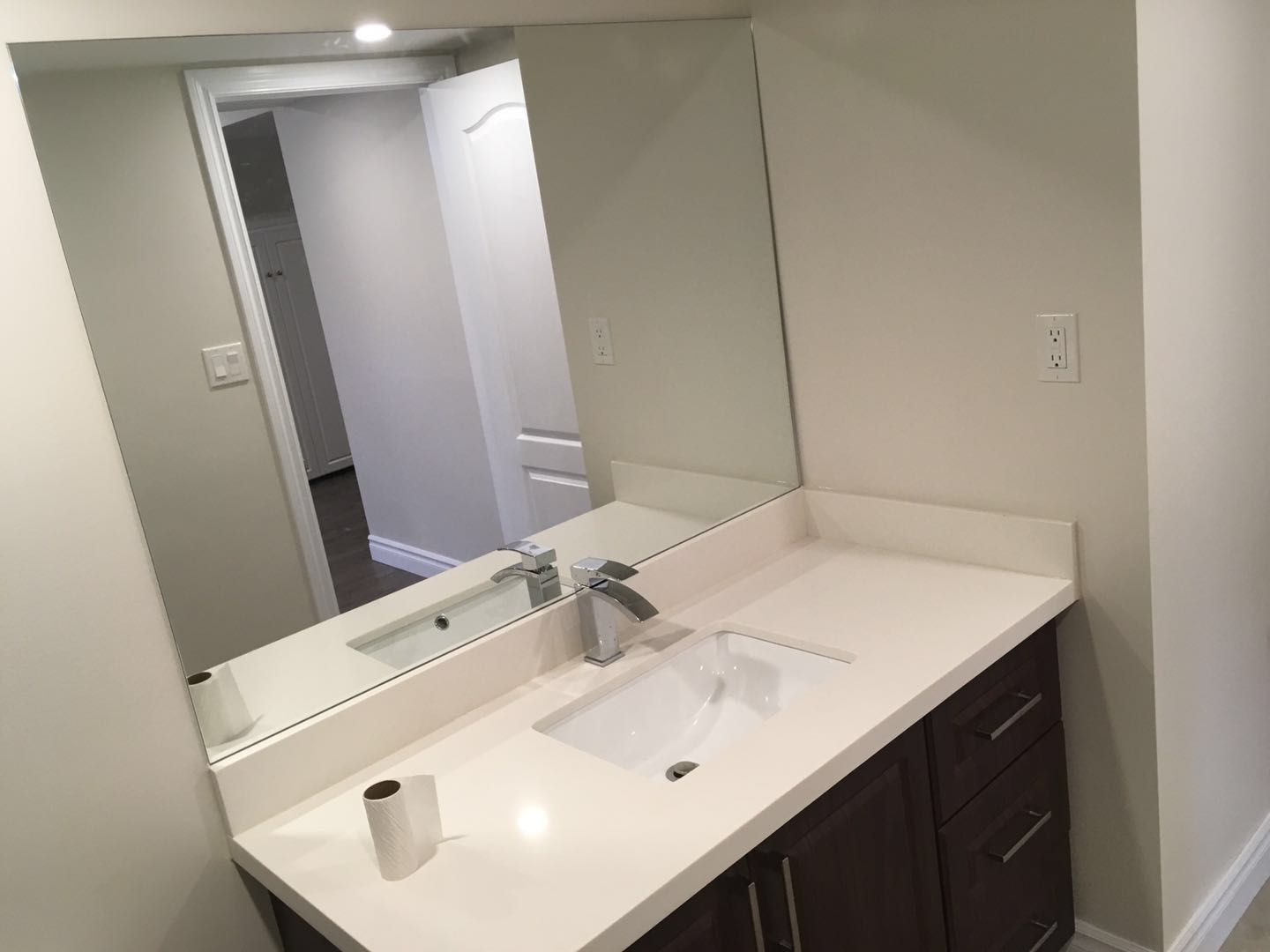 This Toronto interior renovation features a sleek bathroom vanity with a clean white quartz countertop, integrated sink, and a large frameless mirror. The design combines dark wood cabinetry with modern chrome fixtures, creating a simple yet elegant space that is both functional and easy to maintain. Neutral tones and efficient layout enhance brightness and usability.