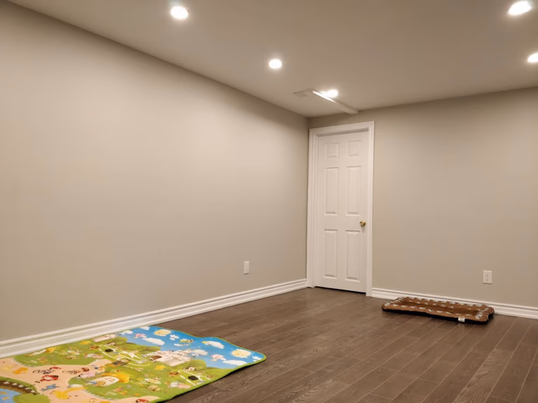 This Scarborough basement renovation project features a newly finished room with modern pot lighting, smooth painted walls, and durable hardwood flooring. The clean layout and warm lighting create a bright and comfortable basement living space, showcasing the craftsmanship of a professional Toronto renovation company.