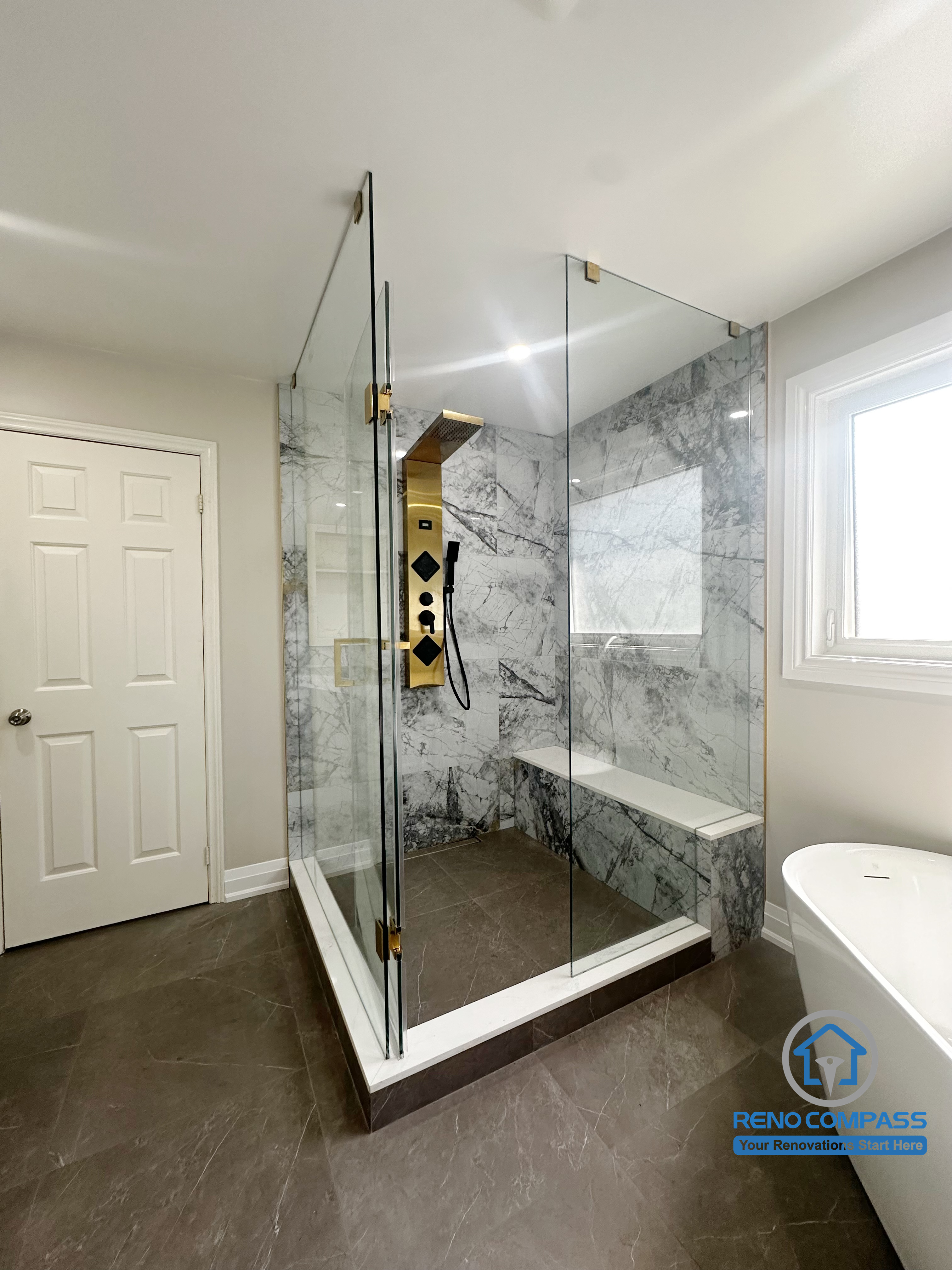 This Oakville bathroom renovation showcases a frameless glass walk-in shower with marble-look wall panels, a built-in bench, and a streamlined shower system. The enclosure is designed to maximize openness while maintaining clear separation between wet and dry zones. Executed by Reno Compass, the shower layout emphasizes durability, comfort, and long-term functionality for everyday use.