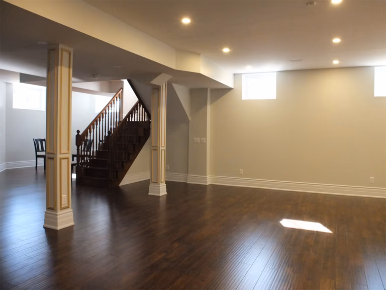 This Richmond Hill basement renovation features a spacious open-concept layout with rich hardwood flooring, custom decorative columns, and modern recessed lighting. The upgraded staircase, neutral wall tones, and clean architectural details create a bright and functional living space ideal for family use and entertaining. Professionally finished to enhance comfort, durability, and home value.