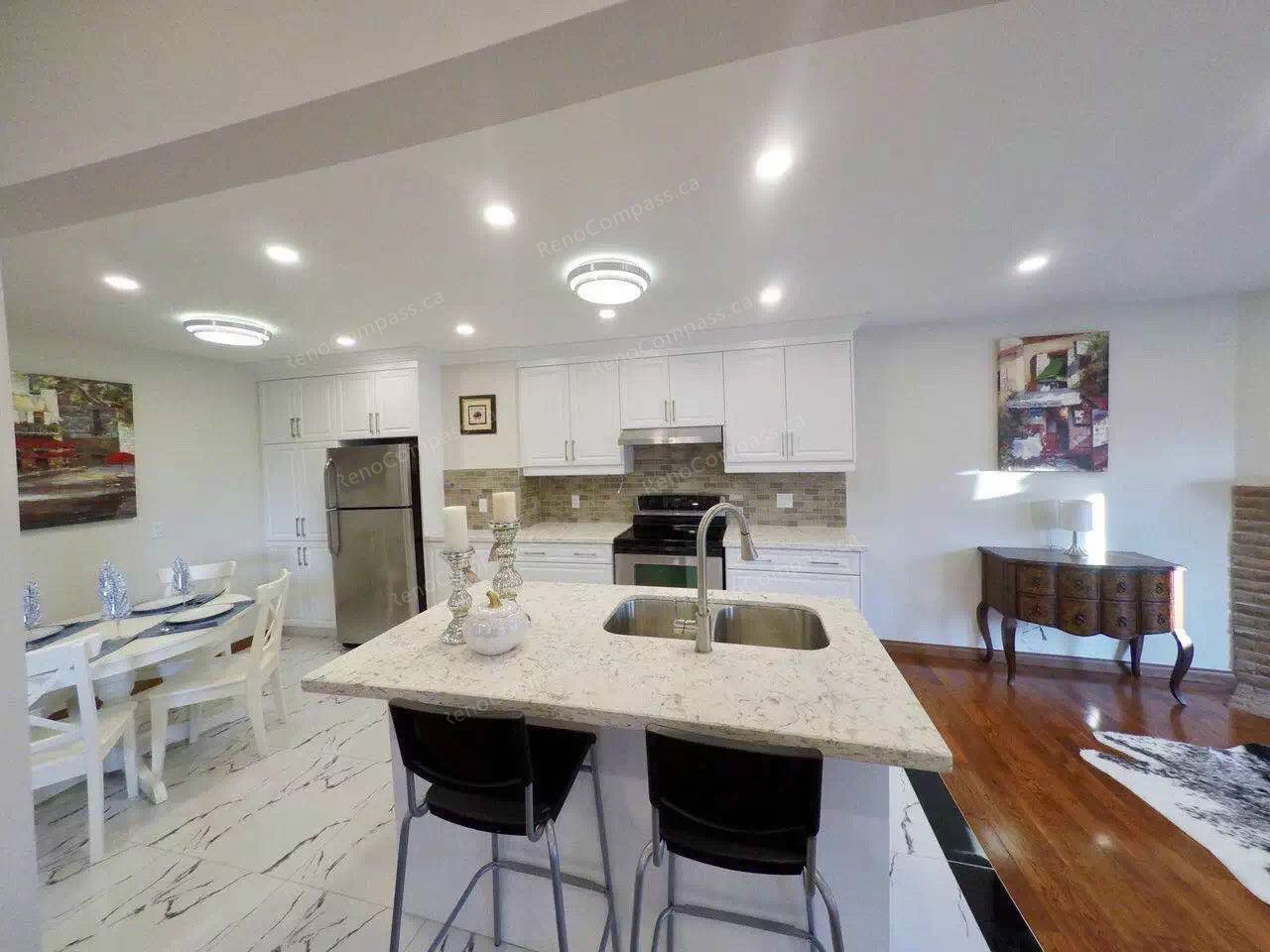 After renovation view of a modern open-concept kitchen in Scarborough featuring white cabinetry, quartz countertops, new tile flooring, upgraded lighting, and a functional island with double sink. Completed by a professional Toronto renovation company, this kitchen renovation enhances brightness, storage, and everyday usability while seamlessly connecting the dining and living areas.