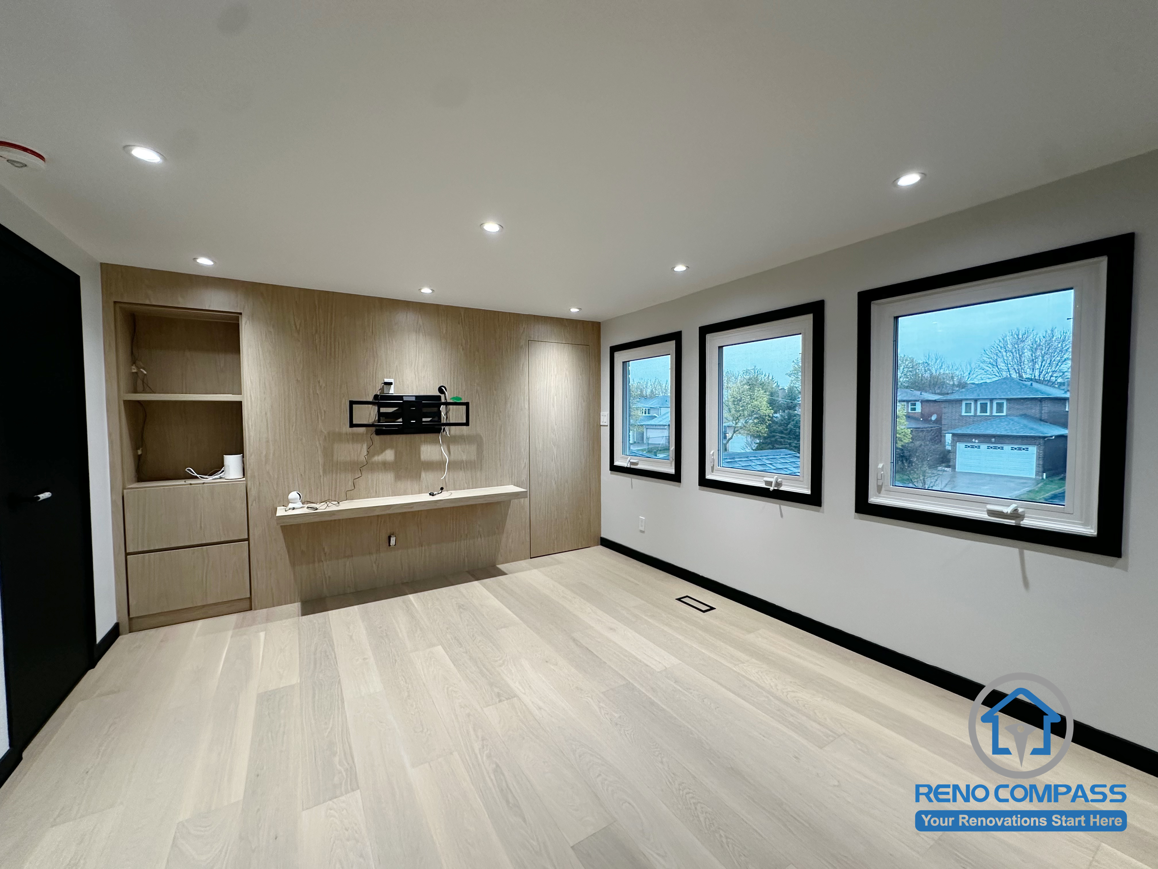 A clean and modern bedroom featuring a custom wood-grain feature wall with built-in shelving and a floating desk.
Large windows bring in abundant natural light, enhancing the warm flooring tones and creating a bright, peaceful living environment. 这是一间以木纹背景墙为亮点的现代卧室，融合开放式置物架与悬浮式书桌设计。
三扇大窗带来自然光线，让浅木地板与整体空间显得更加明亮、温暖、舒适。