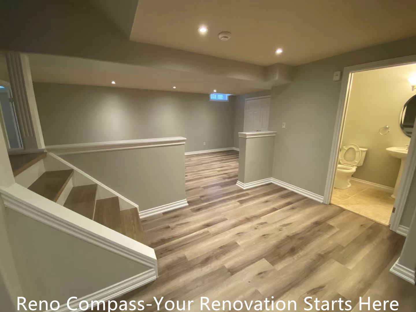 This Oakville interior renovation features a fully finished basement hallway designed to improve flow, comfort, and everyday usability. Continuous wood-look vinyl flooring connects the staircase, main basement area, and bathroom entrance, creating visual consistency throughout the space. Recessed ceiling lights provide balanced illumination, while half-height walls help define circulation zones without making the basement feel enclosed. Neutral wall colors and clean trim details enhance brightness and maintain a modern, cohesive appearance. This thoughtfully planned layout supports multi-purpose basement use and reflects the quality standards of a professional Toronto renovation company.
