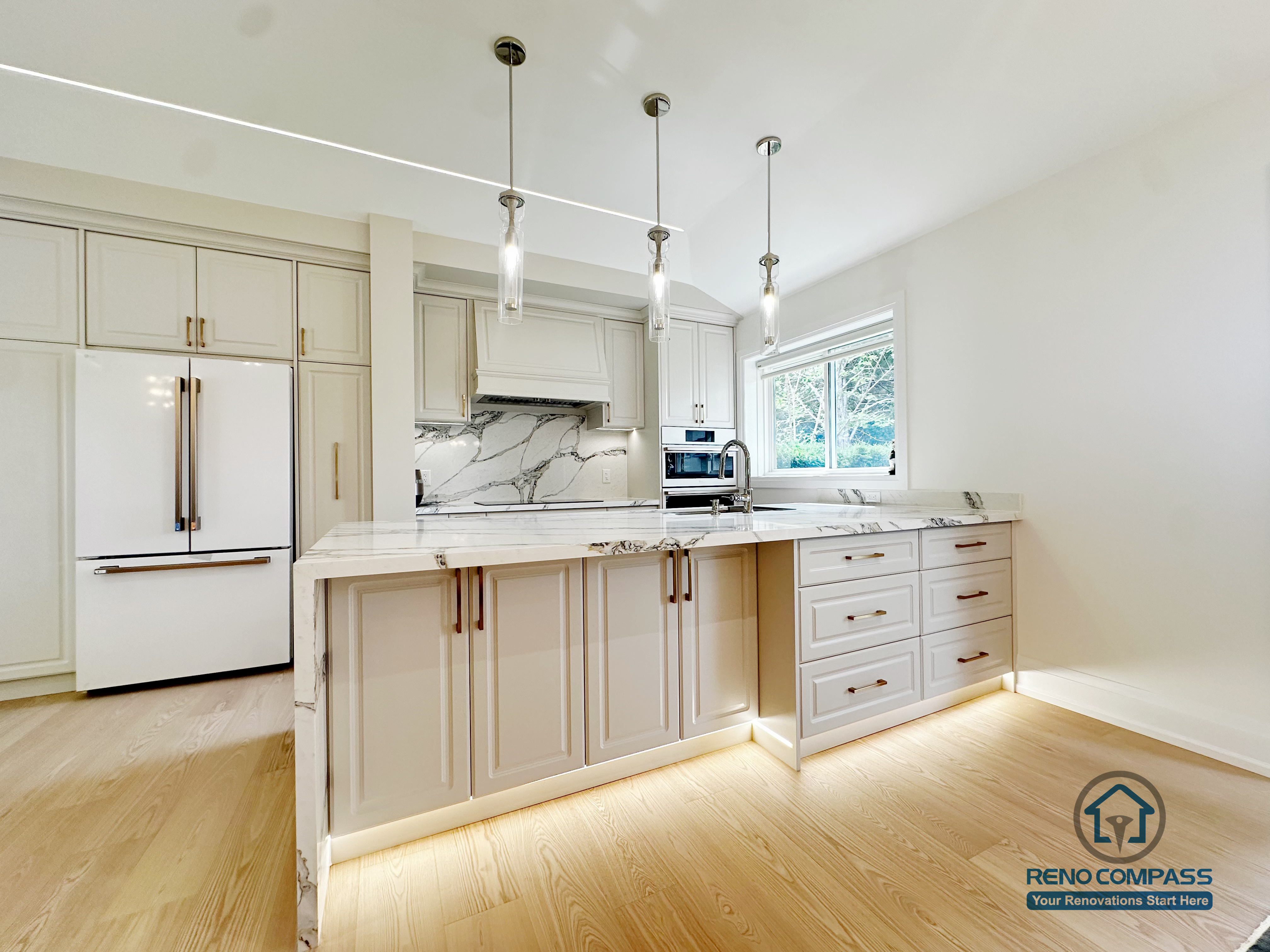 A bright modern kitchen featuring a full waterfall island, marble-look surfaces, and custom cabinetry. Integrated toe-kick lighting and brass hardware add a refined touch, creating a clean and elegant cooking space.
明亮现代的厨房配置全瀑布式中岛、大理石纹台面与定制橱柜。脚踢线灯与金色五金进一步提升质感，打造干净、优雅且实用的烹饪空间。