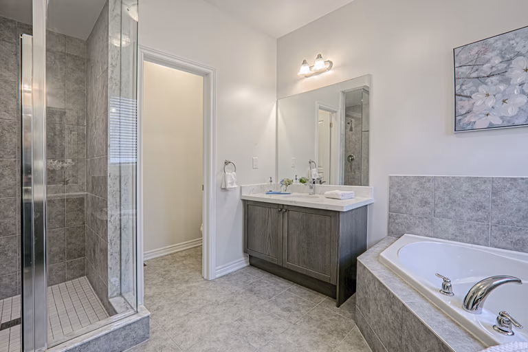 This Toronto luxury master bathroom renovation features a spacious layout with a double vanity, premium stone countertops, and a built-in soaking tub surrounded by elegant tile finishes. The design includes modern lighting, large mirrors, and neutral tones that create a bright and relaxing spa-like environment. Completed by a professional Toronto renovation company, this bathroom project showcases high-quality craftsmanship, functional layout planning, and contemporary residential design tailored for modern comfort.