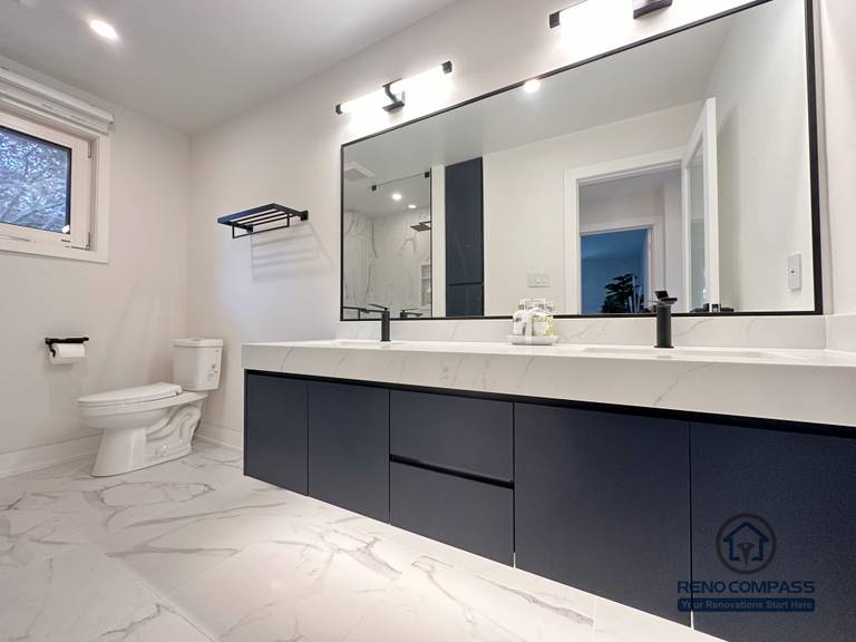 Spacious bathroom renovation in Toronto featuring a custom double-sink vanity, oversized mirror, modern wall-mounted lighting, matte black fixtures, and marble-look porcelain flooring. Designed and completed by a trusted Toronto renovation company with a focus on comfort, storage, and clean contemporary style.