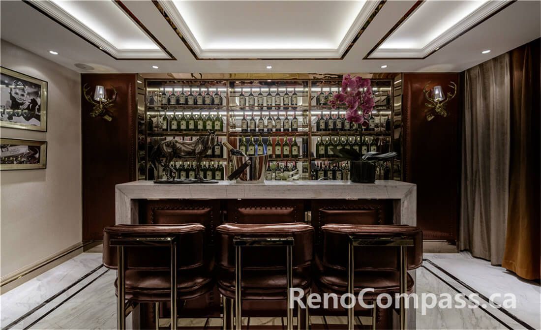 This Toronto interior renovation features a bespoke home bar design with a marble countertop, custom wood cabinetry, and a full-height illuminated wine and liquor display wall. Elegant ceiling lighting, brass accents, and tailored seating create a refined entertainment space perfect for hosting guests. Completed by an experienced Toronto Renovation Company, the project highlights premium finishes, functional layout planning, and sophisticated craftsmanship, delivering a private luxury bar experience within a modern residential setting.