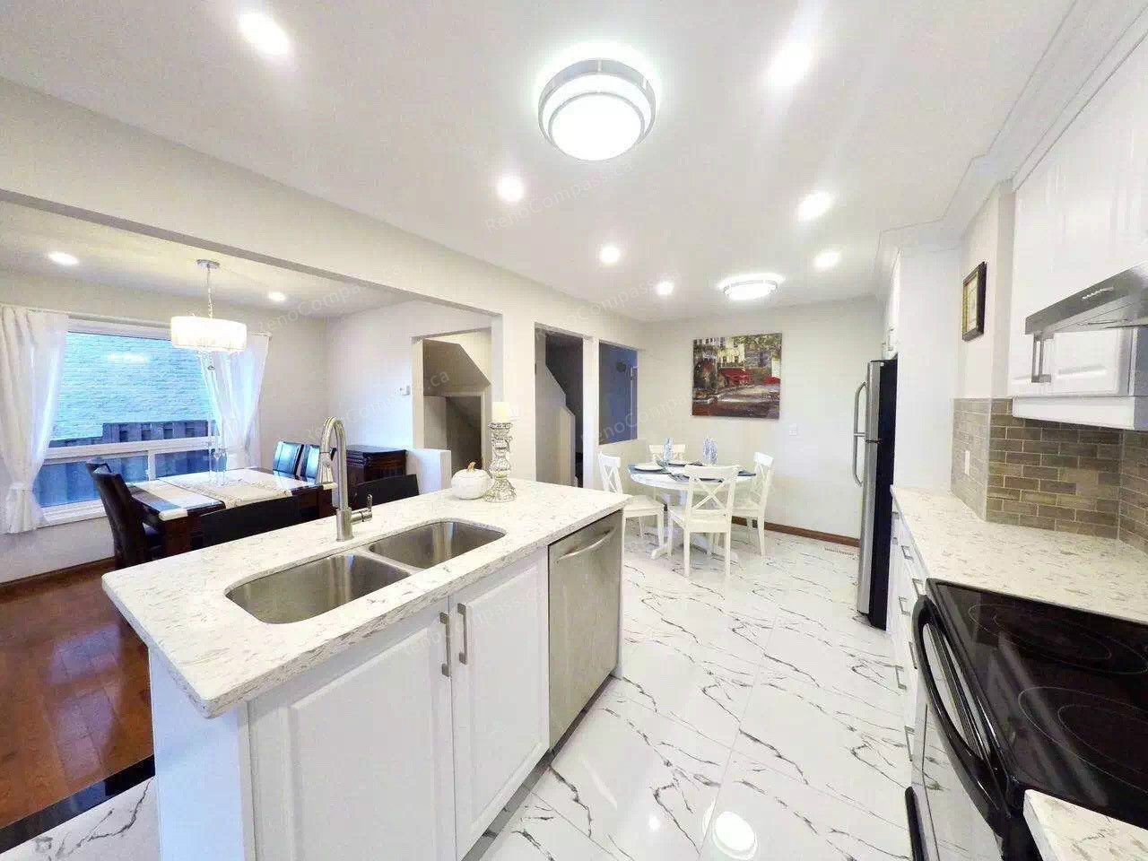 After renovation view of a modern open-concept kitchen in Scarborough featuring white cabinetry, quartz countertops, new tile flooring, upgraded lighting, and a functional island with double sink. Completed by a professional Toronto renovation company, this kitchen renovation enhances brightness, storage, and everyday usability while seamlessly connecting the dining and living areas.