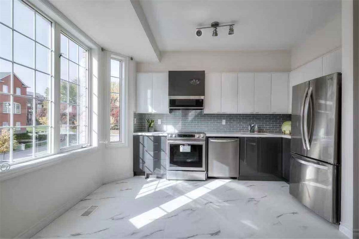 This Thornhill interior renovation showcases a bright and modern kitchen featuring glossy white cabinetry, stainless steel appliances, grey tile backsplash, and elegant marble-style flooring. Large bay windows bring in abundant natural light, enhancing the open and spacious feel of the home. Completed by a professional Toronto renovation team, this upgrade delivers a clean, contemporary interior designed for both comfort and functionality.