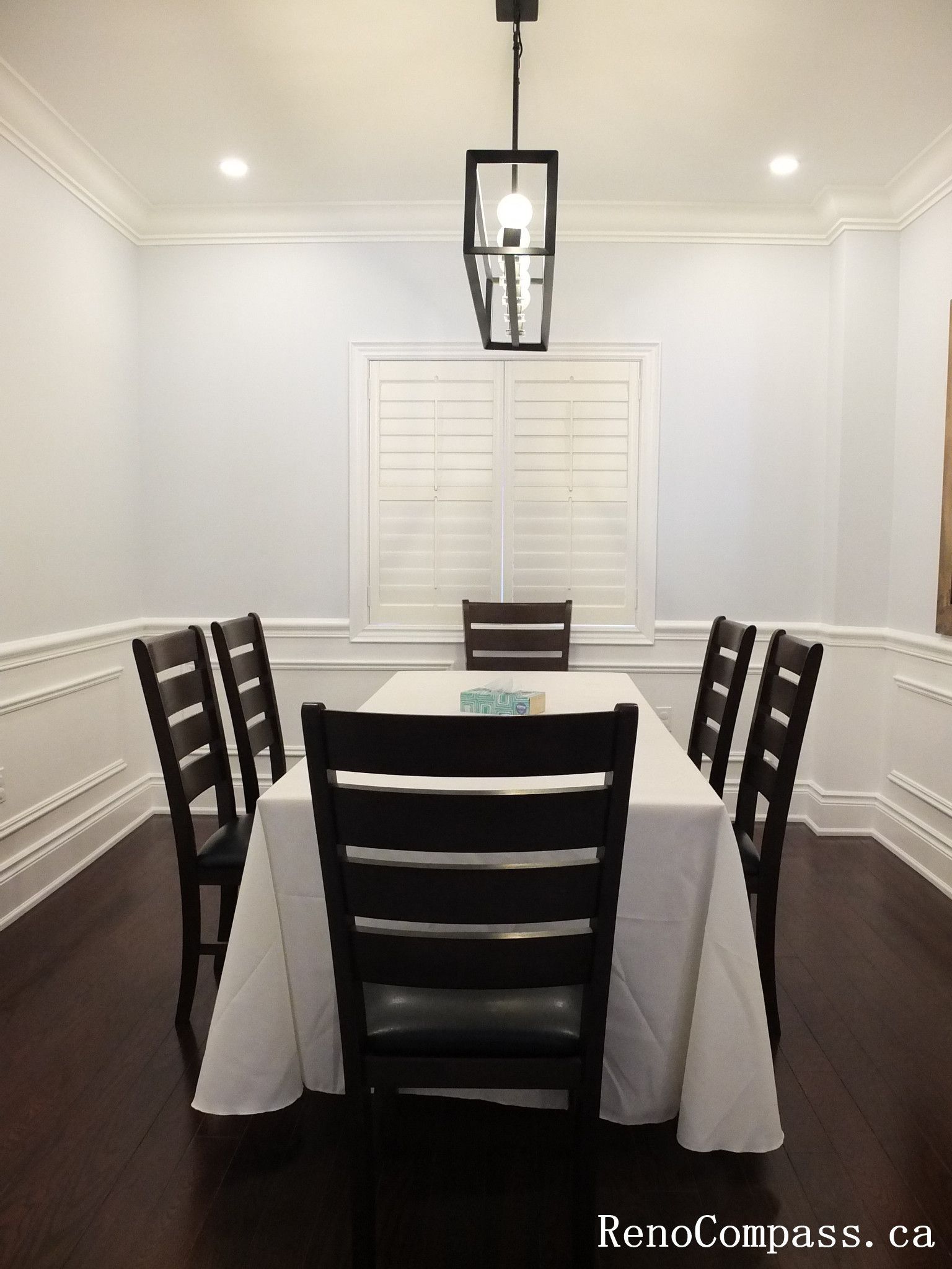 This Newmarket interior renovation showcases a warm and inviting dining room designed for family gatherings and everyday meals. The space features elegant wall paneling (wainscoting), dark hardwood flooring, and a modern pendant light centered above the dining table to create a balanced and comfortable atmosphere. Large windows with shutters allow natural light to brighten the room while maintaining privacy. Completed by Reno Compass Inc., this project highlights refined interior finishing and thoughtful design that enhances both functionality and style in a modern home.