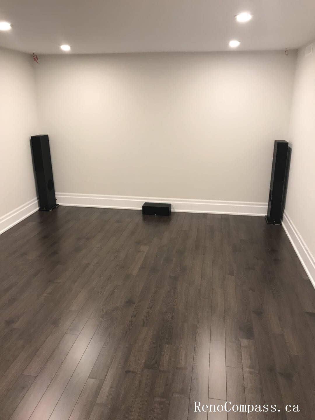 This image features a newly finished basement bedroom in Richmond Hill, showcasing dark hardwood flooring, fresh neutral wall paint, upgraded baseboards, and bright overhead lighting. Renovated by Reno Compass Inc., the space is designed to feel clean, modern, and move‑in ready.