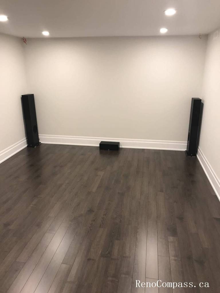 This image features a newly finished basement bedroom in Richmond Hill, showcasing dark hardwood flooring, fresh neutral wall paint, upgraded baseboards, and bright overhead lighting. Renovated by Reno Compass Inc., the space is designed to feel clean, modern, and move‑in ready.