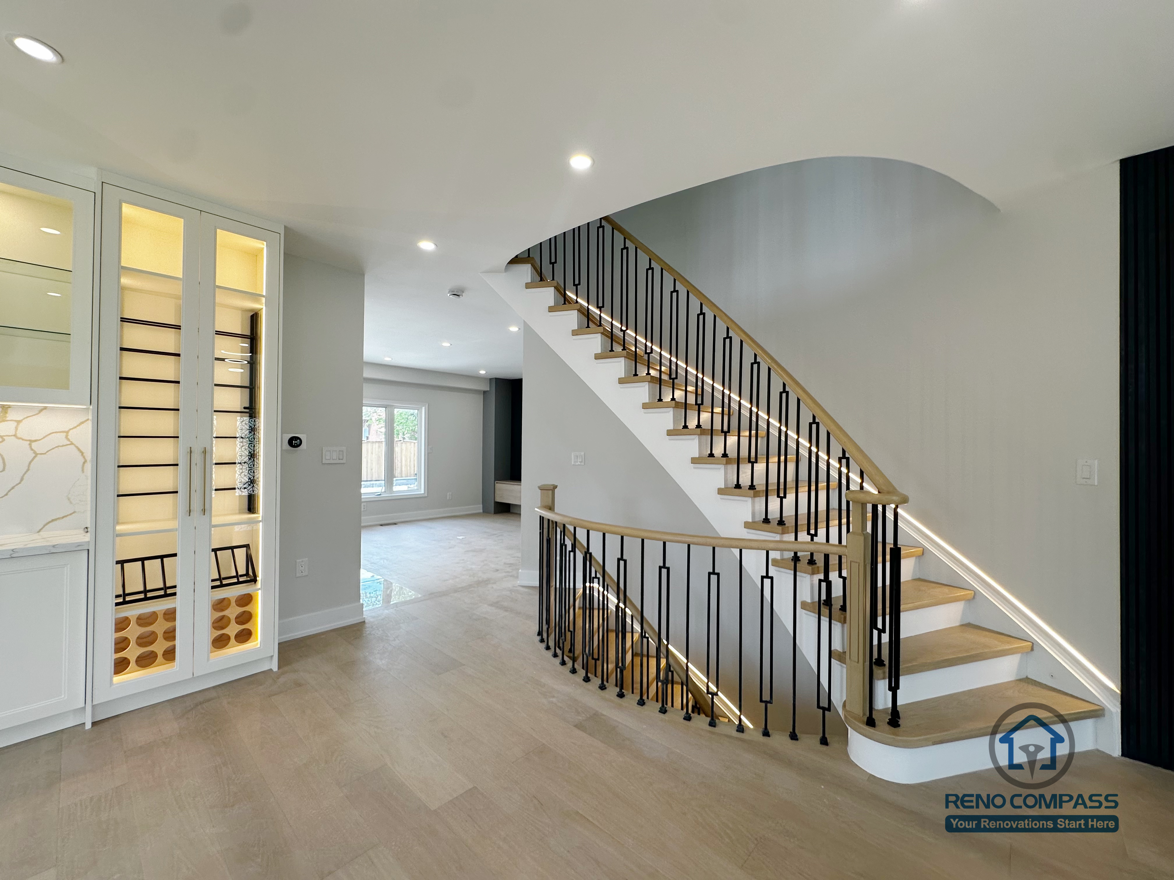This image showcases the staircase and open living area from a Markham interior renovation project, where spatial flow and visual continuity were key design priorities. The staircase features light wood treads paired with black metal railings, creating a clean contrast that adds definition without overwhelming the space. Integrated LED lighting along the steps enhances both safety and atmosphere.

The open layout allows natural light to travel freely across the main floor, visually connecting the staircase, adjacent cabinetry, and living areas. Neutral finishes and consistent material selections help unify the different zones while maintaining a calm, modern aesthetic.

Careful attention to proportions, circulation, and lighting ensures the space feels open yet well-structured. This design reflects Reno Compass’s approach to interior renovations—balancing architectural clarity, everyday functionality, and refined detailing for Markham homes.