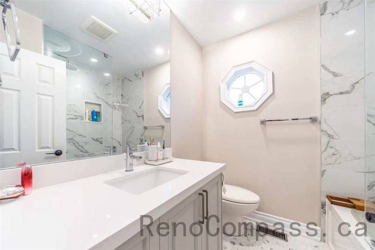 This North York interior renovation features a bright and elegant bathroom upgrade with a modern quartz vanity, large mirror, and marble-style tile shower enclosure. The design includes a glass shower, clean white cabinetry, and contemporary fixtures that create a fresh and luxurious atmosphere. Completed by a professional Toronto renovation company, this bathroom renovation combines refined materials and functional design to deliver a comfortable and stylish space.