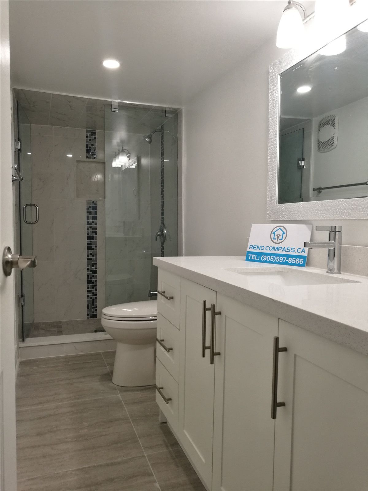 Bathroom renovation project in Pickering featuring a modern white vanity with quartz countertop, undermount sink, large mirror, and a frameless glass shower enclosure. The neutral tile flooring and clean layout enhance brightness and functionality, completed by a professional Toronto renovation company.