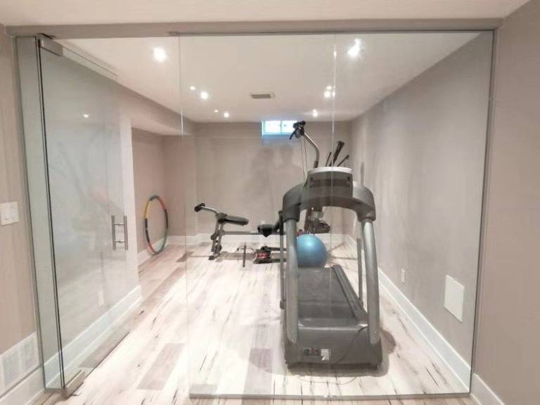 This Richmond Hill interior partial renovation showcases a modern basement home gym upgrade featuring a full glass partition wall, recessed ceiling lighting, and durable light-tone flooring. The space was redesigned to create a bright and functional fitness area while maintaining a clean, contemporary interior style. This basement renovation enhances usability and adds lifestyle value to the home, providing a dedicated workout space with improved lighting, layout, and finishing details. Completed by Reno Compass, this project highlights professional interior remodeling services across Richmond Hill and the Greater Toronto Area.