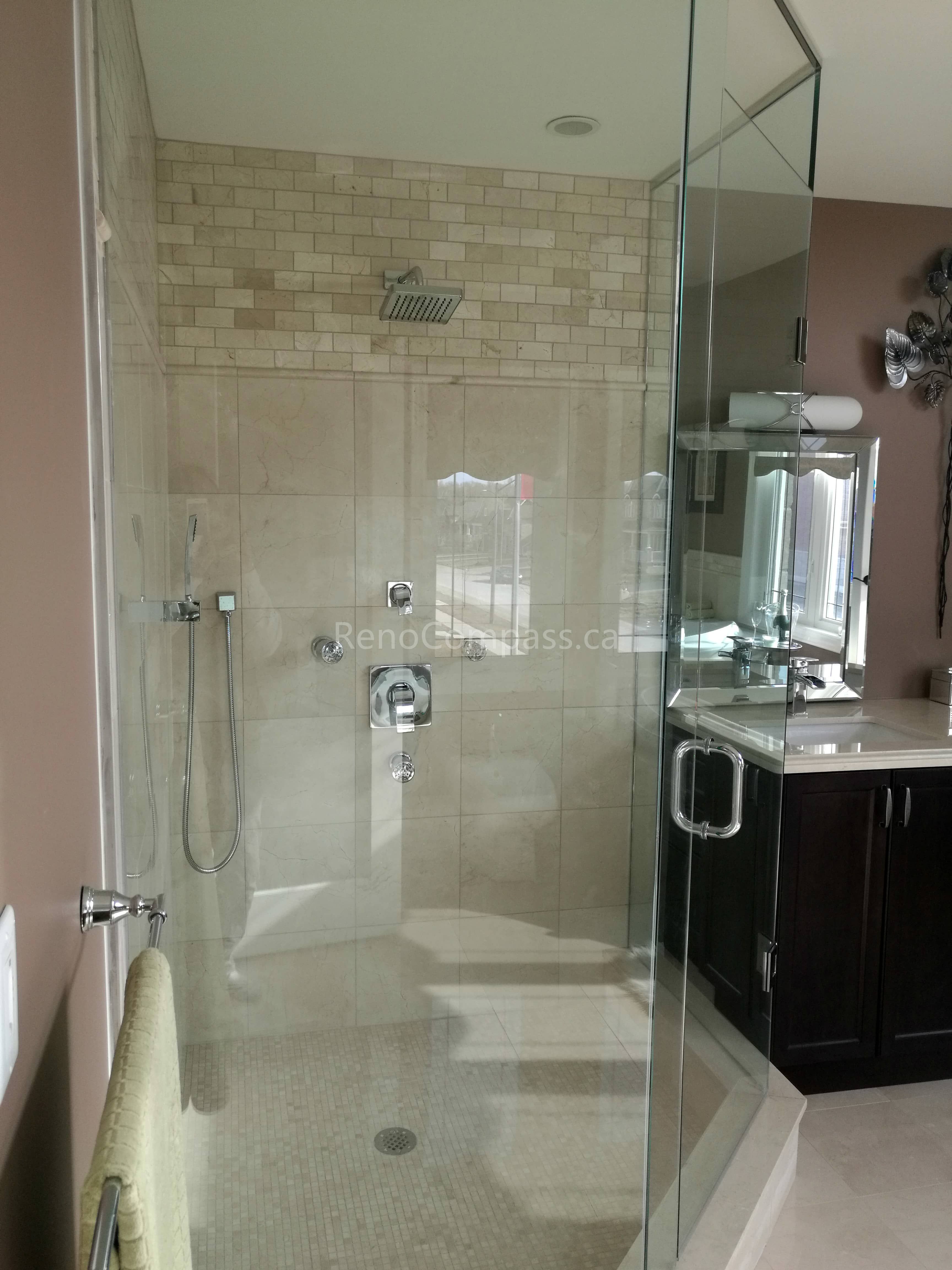 This image features a walk-in glass shower completed as part of a Toronto interior renovation project. The shower is finished with neutral-toned wall tiles and a mosaic tile floor, creating a clean and cohesive look. A frameless glass enclosure enhances openness while allowing natural light to flow through the space. Integrated fixtures and a ceiling-mounted showerhead add both functionality and modern comfort. This bathroom renovation highlights careful detailing, durable materials, and high-quality craftsmanship tailored to Toronto residential interiors.