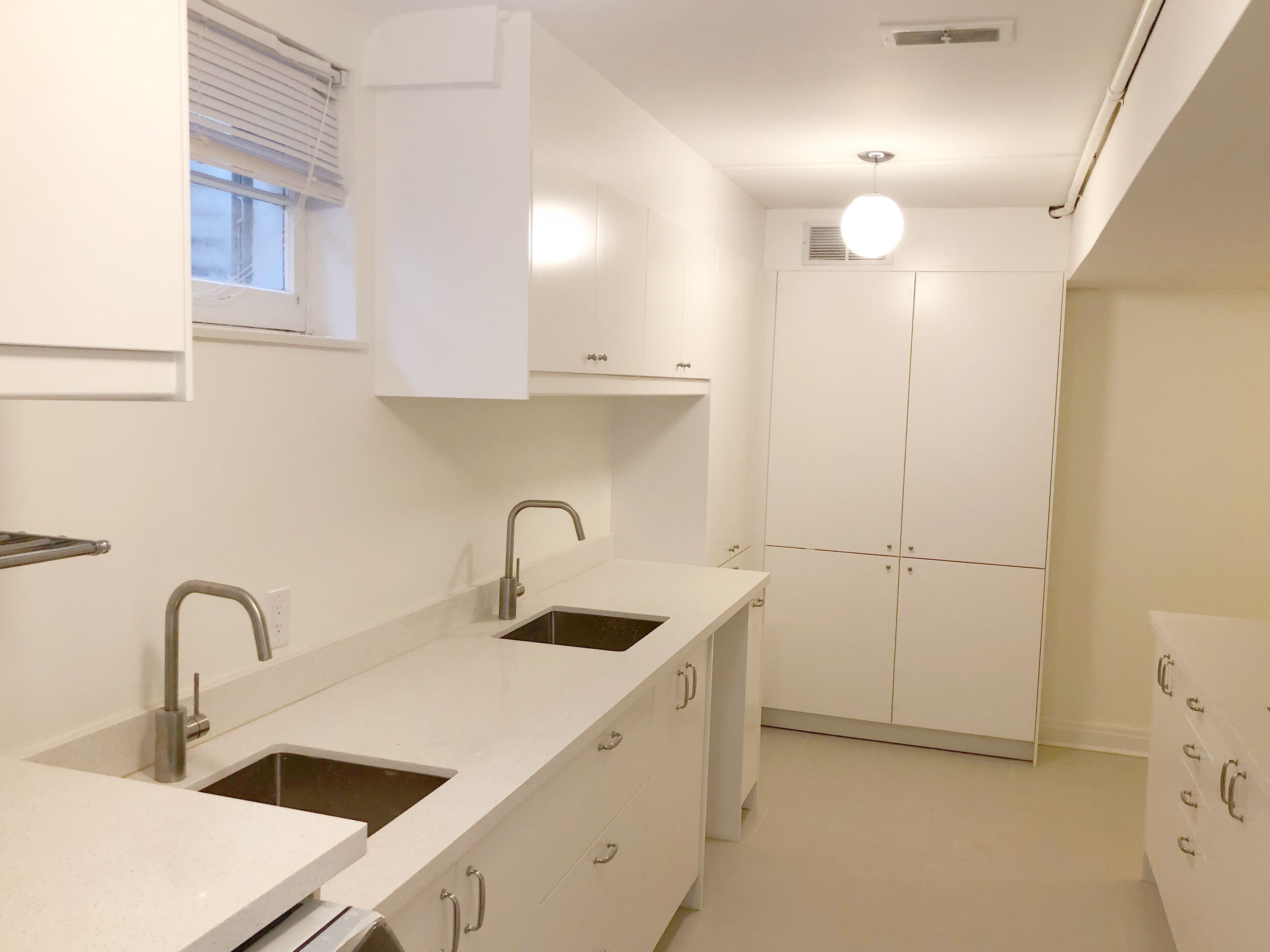 This Etobicoke interior renovation features a custom-designed laundry and utility room with double stainless steel sinks, durable quartz countertops, and full-height storage cabinetry for maximum organization. The clean white cabinetry and modern fixtures create a bright and functional workspace, while practical layout planning improves efficiency for daily household tasks. Completed by Reno Compass Inc., this renovation enhances storage, usability, and long-term durability with a clean and timeless design.
