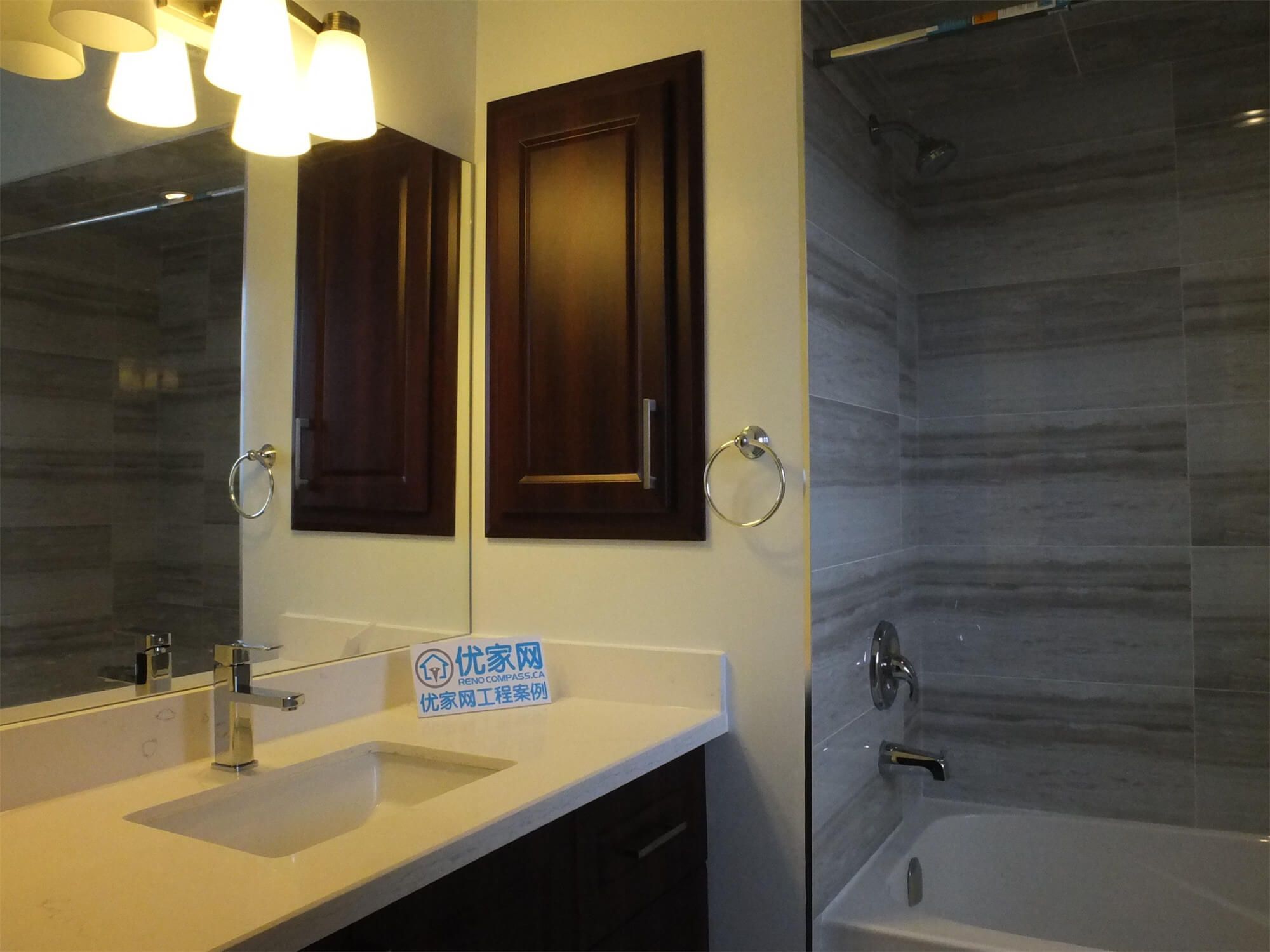 This photo showcases a finished bathroom as part of a North York interior renovation, featuring a modern vanity with integrated sink, dark wood cabinetry, quartz countertop, and a clean tub-shower combination with large-format wall tiles. The design balances functionality and durability, making it suitable for everyday family use while maintaining a timeless, contemporary look.