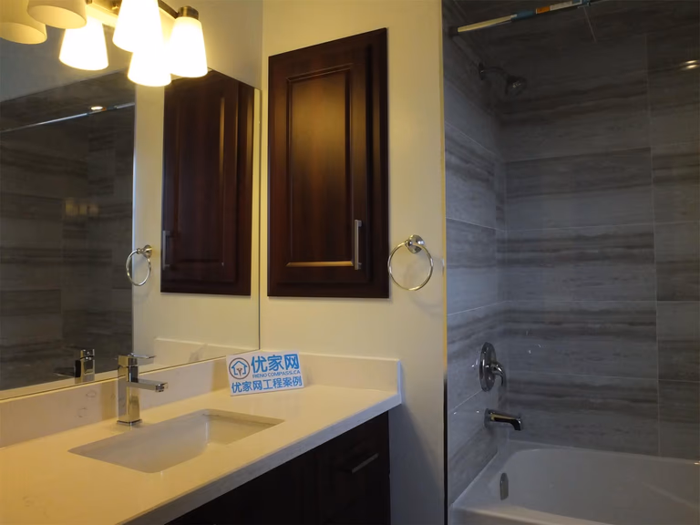 This photo showcases a finished bathroom as part of a North York interior renovation, featuring a modern vanity with integrated sink, dark wood cabinetry, quartz countertop, and a clean tub-shower combination with large-format wall tiles. The design balances functionality and durability, making it suitable for everyday family use while maintaining a timeless, contemporary look.