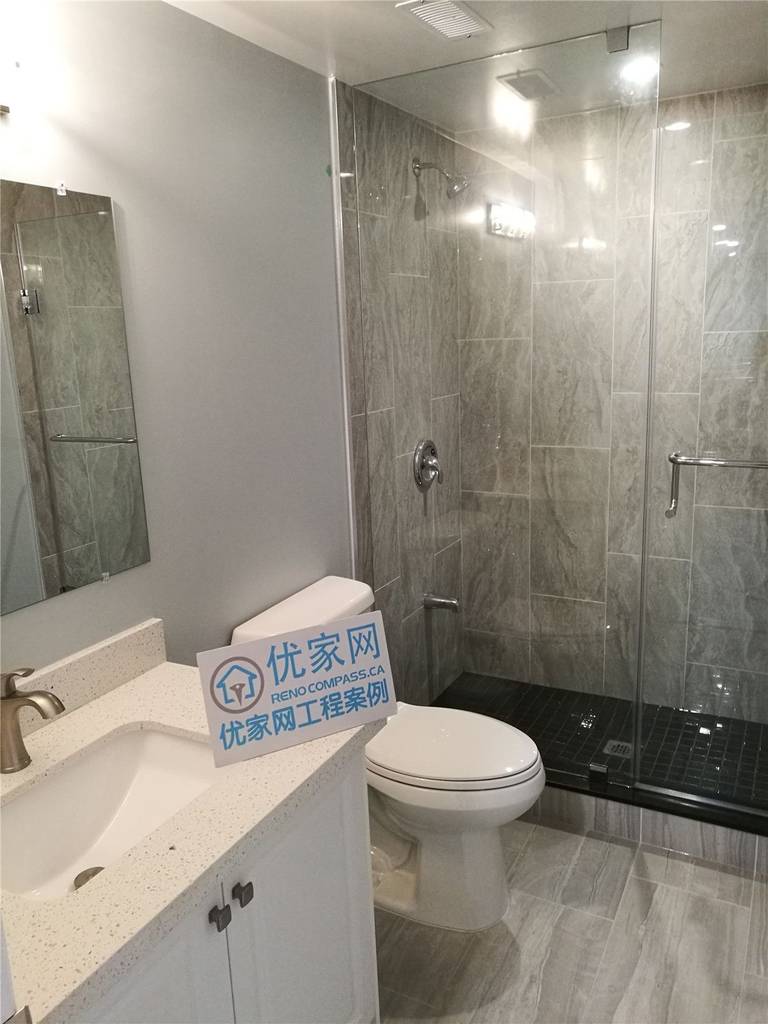 This image showcases a completed basement bathroom as part of a North York interior renovation project. The space features a modern glass-enclosed shower, large-format grey wall tiles, matching floor tiles, and a clean white vanity with an integrated sink. Recessed lighting and a frameless glass shower door enhance brightness and visual openness, while the layout prioritizes functionality and ease of maintenance. This North York interior renovation reflects clean workmanship, durable material selection, and practical bathroom design by a professional Toronto renovation company.